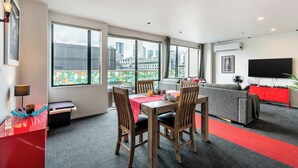 A modern hotel room with a dining area, a sofa, a TV, and large windows offering city views. - Auckland Penthouse: SkyTower Views. Special Offer (Auckland)