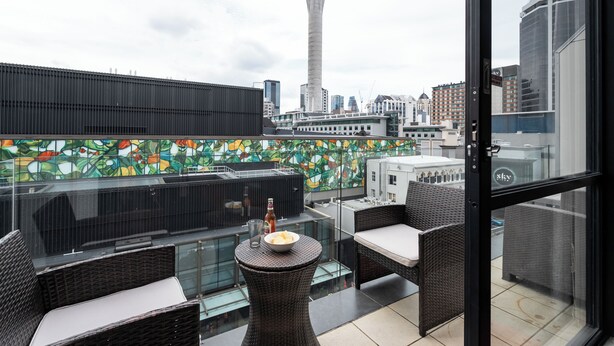 A rooftop terrace with wicker furniture, a glass table, and a view of a tower and cityscape. - Auckland Penthouse: SkyTower Views. Special Offer (Auckland)