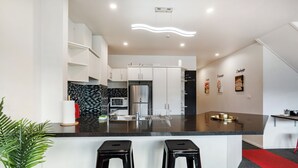 A modern kitchen with white cabinets, a black countertop, stainless steel appliances, and a red carpet leading to a bar area with two stools. - Auckland Penthouse: SkyTower Views. Special Offer (Auckland)