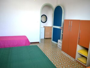 Ein Zimmer mit einem Bett, einem Kleiderschrank, einer kleinen Kommode und einer Tür mit einem runden Gegenstand an der Wand.