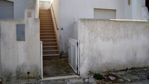 Un escalier étroit mène à un palier surmonté d’une grille métallique, le tout étant entouré de murs blancs avec une base en béton.