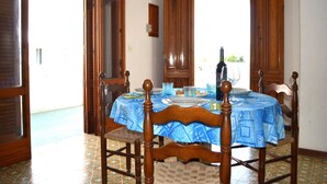 Un coin repas avec une table dressée pour deux personnes, des chaises en bois, une nappe bleue et une bouteille de vin.
