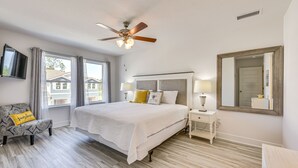 Un dormitorio con cama, mesitas de noche, ventilador de techo, televisor y ventanas amplias.