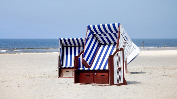 Sillas de playa con fundas azules y blancas a rayas, armazones de madera y un letrero de metal con texto.