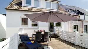 Una casa con un patio, una silla de lounge, una mesa con sillas y una sombrilla.