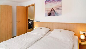 Een hotelkamer met een bed, een houten kledingkast, een nachtkastje met een lamp en een aan de muur hangend schilderij.