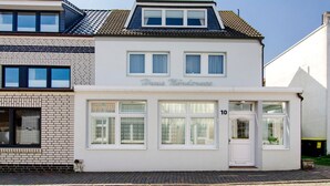 Een gebouw met twee verdiepingen, een witte gevel, een zichtbare winkelentree met het nummer '10' en een heldere lucht.