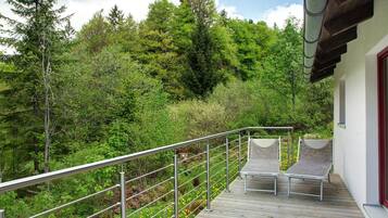 Une terrasse en bois avec des rampes en métal, deux chaises longues et une vue sur une colline boisée.
