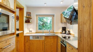 A modern kitchen with wooden cabinets, stainless steel appliances, and a window with a view of greenery. - Holiday Home 'Berghütte Waldhäuser' with Mountain View, Private Terrace and Wi-Fi (Neuschönau)