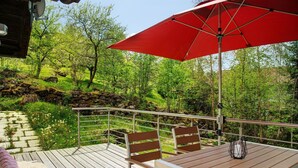 A wooden deck with a red umbrella, metal railing, and a table with chairs. - Holiday Home 'Berghütte Waldhäuser' with Mountain View, Private Terrace and Wi-Fi (Neuschönau)