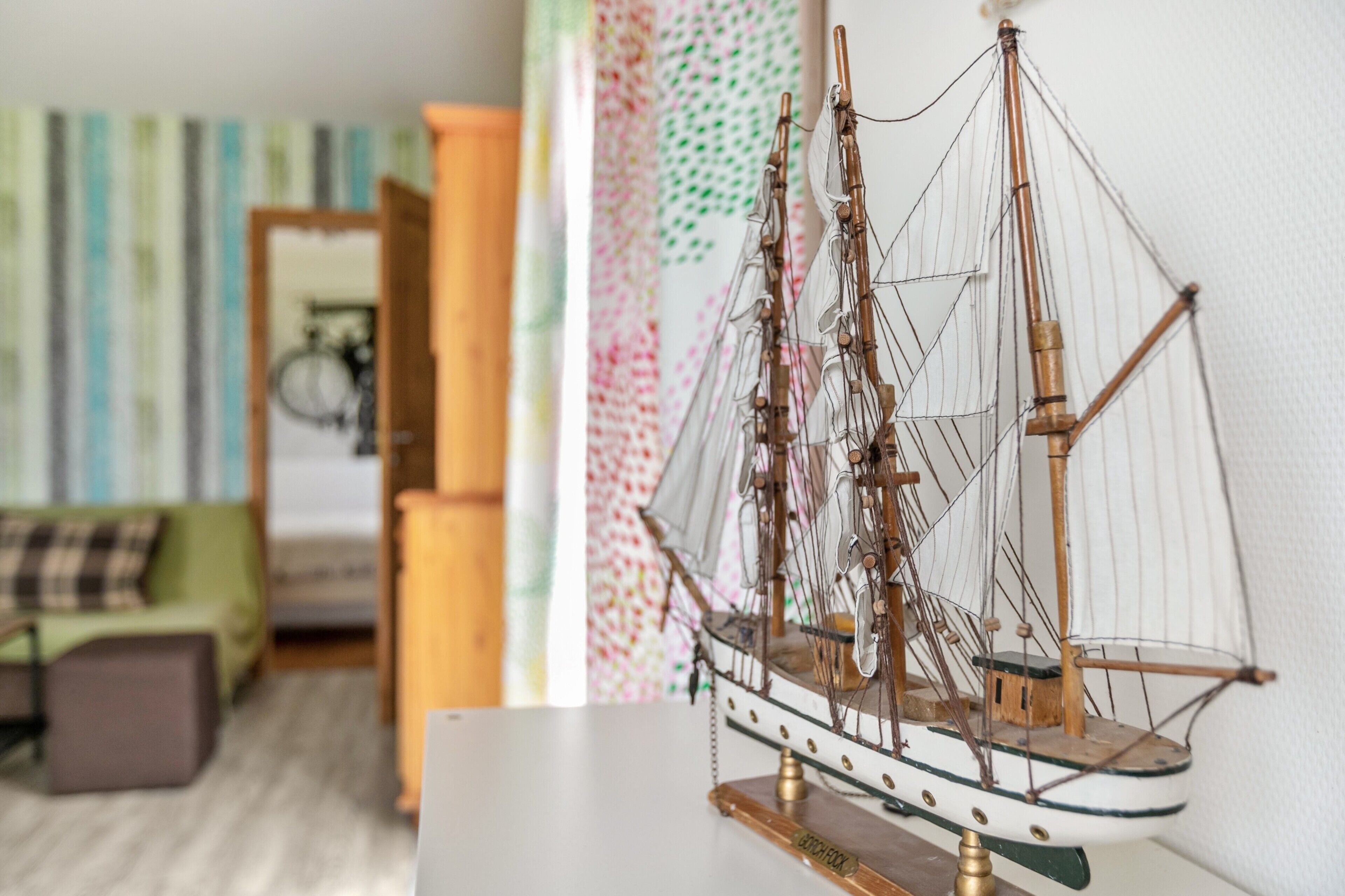 Ein Modellschiff auf einem Tisch in einem Zimmer mit Streifenmuster-Tapete und einem grünen Sofa.