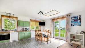 A modern kitchen with a dining area, green cabinets, a flat-screen TV, and a large window with a view. - Holiday Apartment 'Erika' – Quiet Location with Large Garden near the Baltic Sea & Schlei (Saustrup)