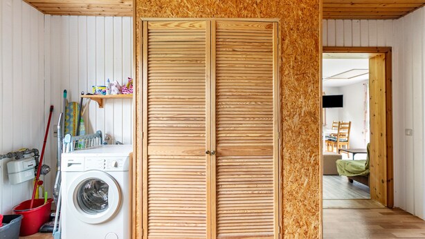 A laundry area with a washing machine, wooden doors, and a red bucket. - Holiday Apartment 'Erika' – Quiet Location with Large Garden near the Baltic Sea & Schlei (Saustrup)