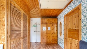 A hallway with wooden walls and floors, a door with a coat hanging, and a blue couch. - Holiday Apartment 'Erika' – Quiet Location with Large Garden near the Baltic Sea & Schlei (Saustrup)