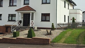 A two-story house with a front porch, a small garden, and a wooden fence.