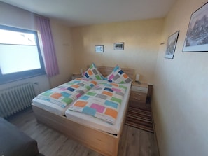 A bedroom with a bed, a nightstand, a window with curtains, and a radiator.