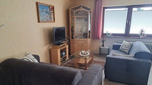 A living room with a sofa, a television, a cabinet, and a window with blinds.