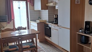 A compact kitchen with a dining table, chairs, a coffee maker, and a refrigerator.