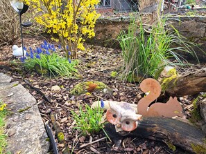 A garden with a variety of plants, a decorative owl, and a metal fence. - Pension Andrea: Apartment 3 with Wi-Fi (Herbstein)