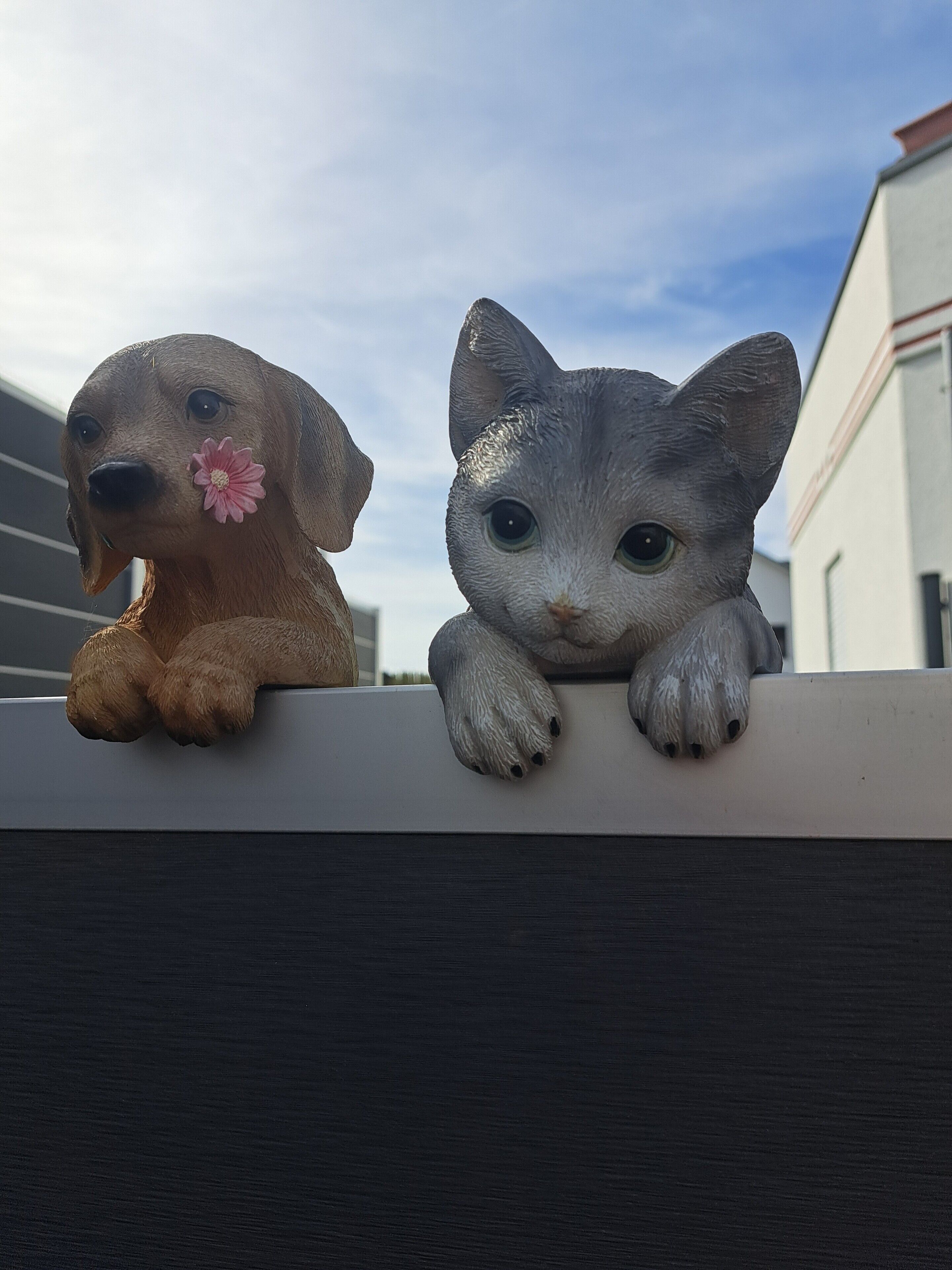 Dos figuras de animales, una que parece un perro y otra un gato, sobre un repisa.