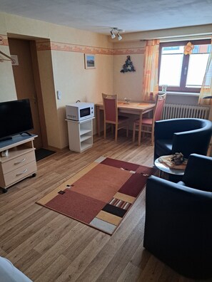 A compact living space with a television, a microwave, a dining table, and two chairs.