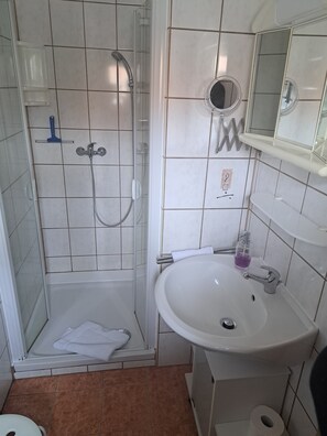A bathroom with a glass-enclosed shower, a white sink with a mirror above it, and a toilet. - Pension Andrea: Apartment 3 with Wi-Fi (Herbstein)