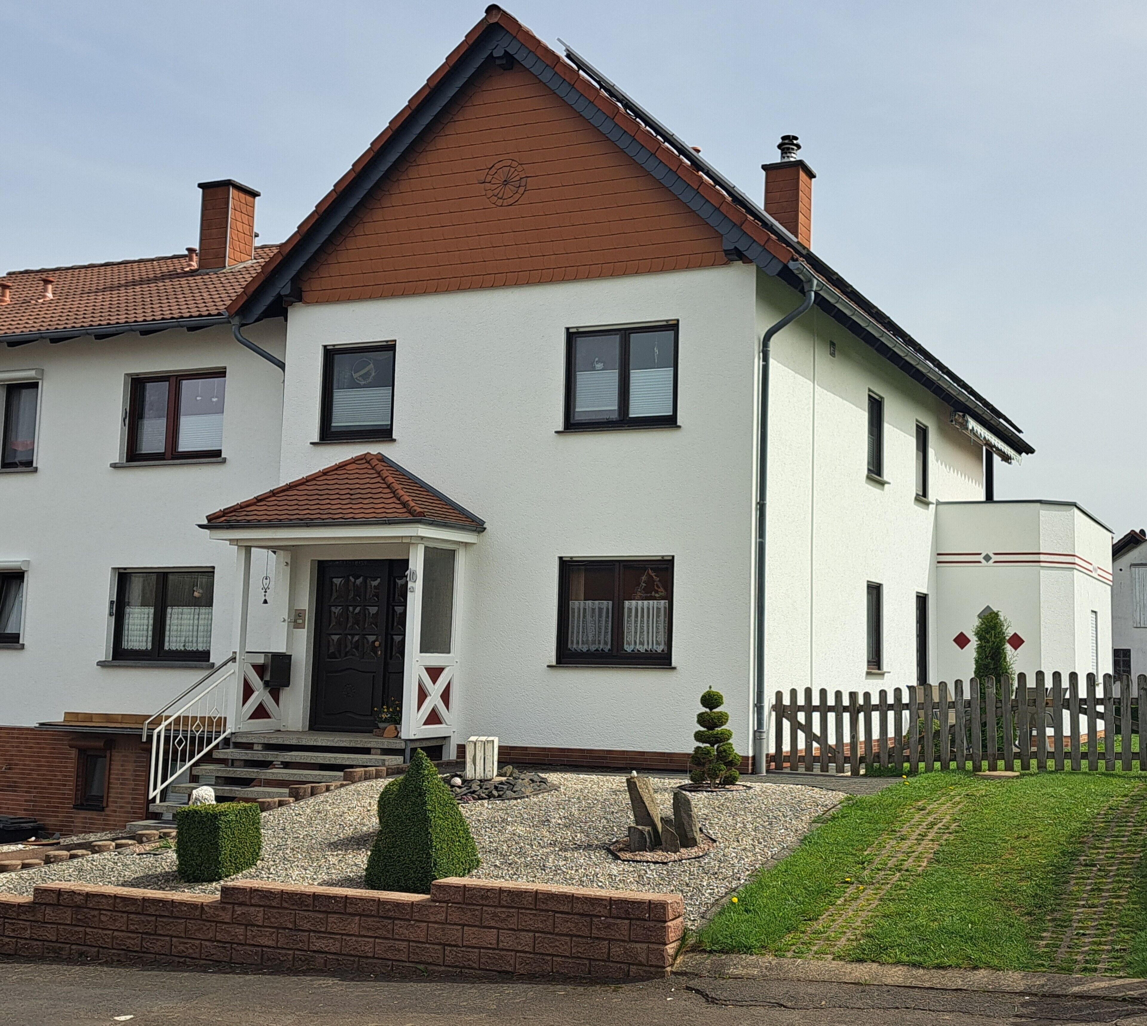 A two-story house with a front porch, a small garden, and a wooden fence.