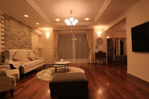 A living room with a brick wall, a sofa, a round coffee table, and a chandelier. - Maccha House Nagano Zenko-ji (Nagano)
