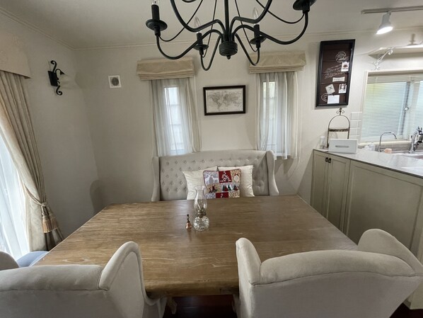 A dining area with a wooden table, white upholstered chairs, a chandelier, and a kitchen area with a sink and cabinets. - Maccha House Nagano Zenko-ji (Nagano)