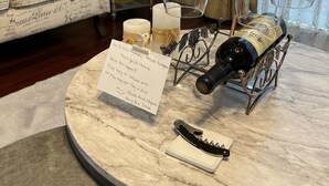 A marble table with wine glasses, a bottle of wine, and a note. A lamp and a chair are in the background. - Maccha House Nagano Zenko-ji (Nagano)
