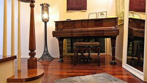 A grand piano in a spacious room with a wooden staircase and a rug on the floor. - Maccha House Nagano Zenko-ji (Nagano)