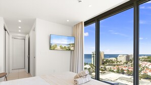 Ein modernes Hotelzimmer mit einem großen Bett, einem an der Wand montierten Fernseher und Blick auf Stadt und Meer durch große Fenster.