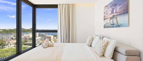 A modern hotel room with a large bed, a city view, and a painting on the wall.