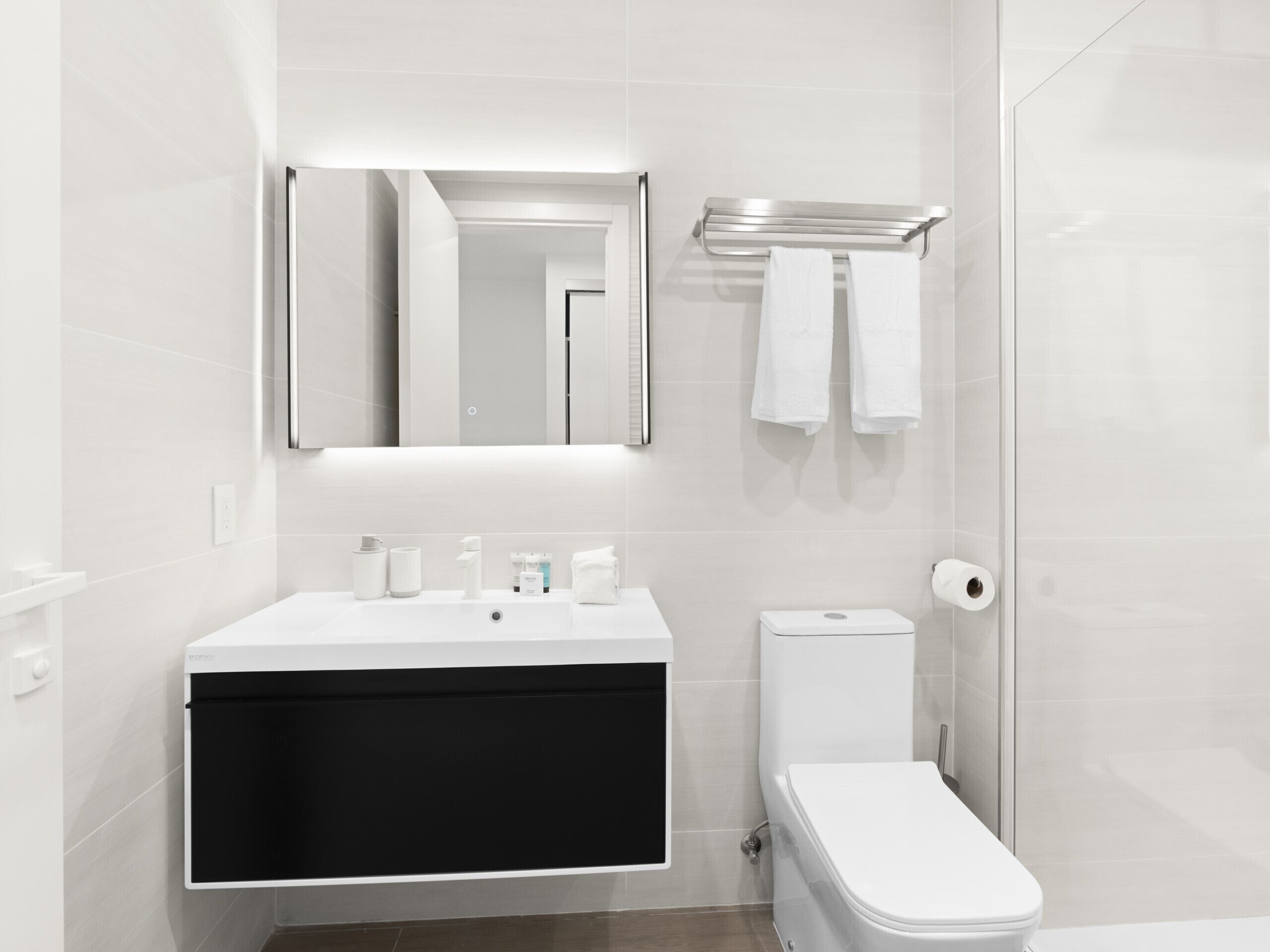 A modern bathroom with a white sink, black vanity, white toilet, and a mirror above the sink.