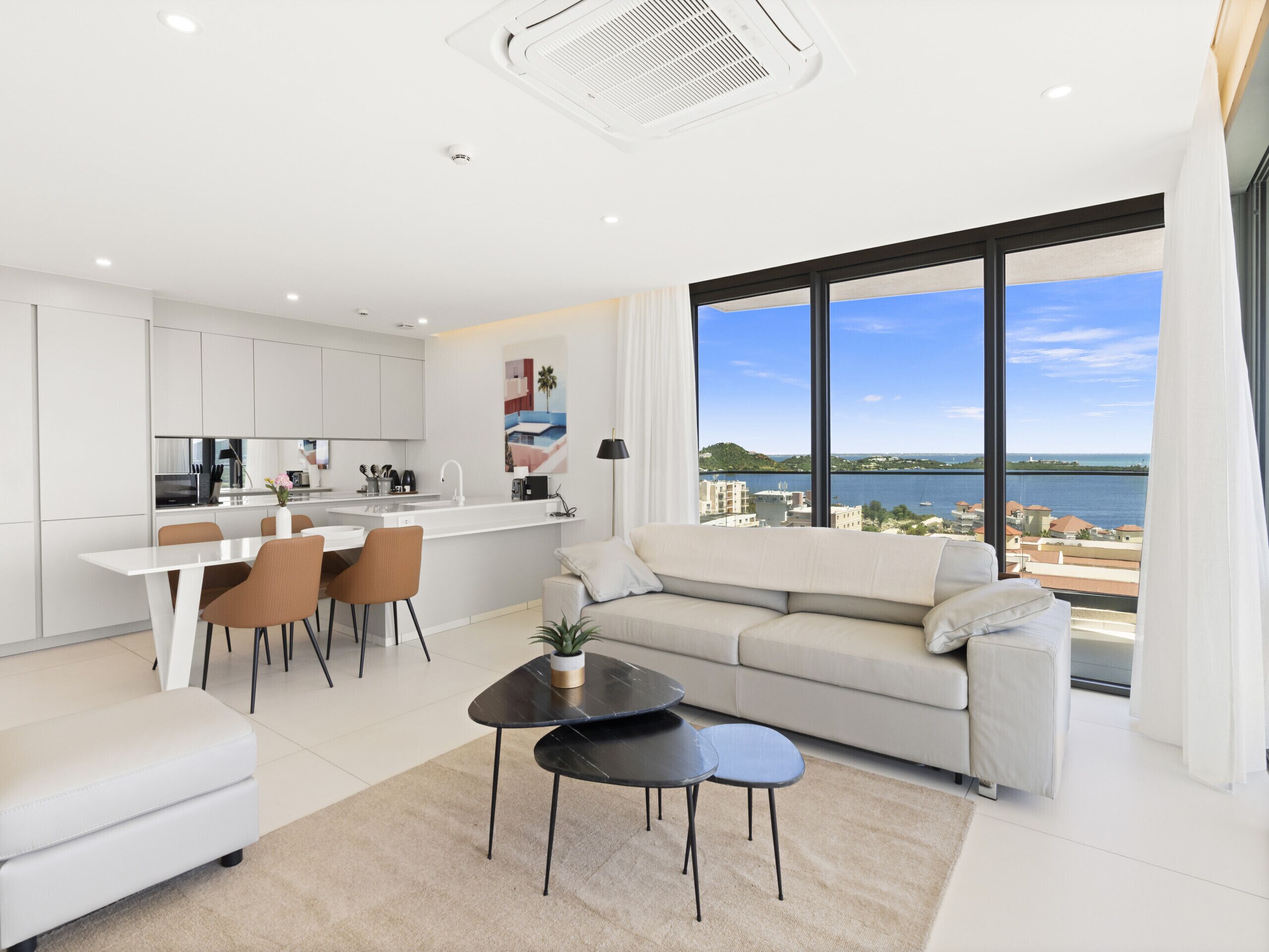 A modern apartment with a kitchen, dining area, and a large window with a city and water view.
