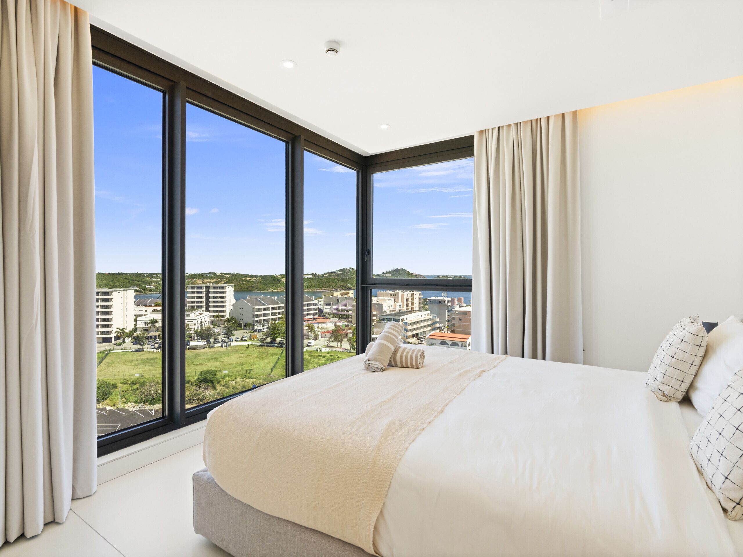 A modern hotel room with a large bed, a view of the city, and large windows.