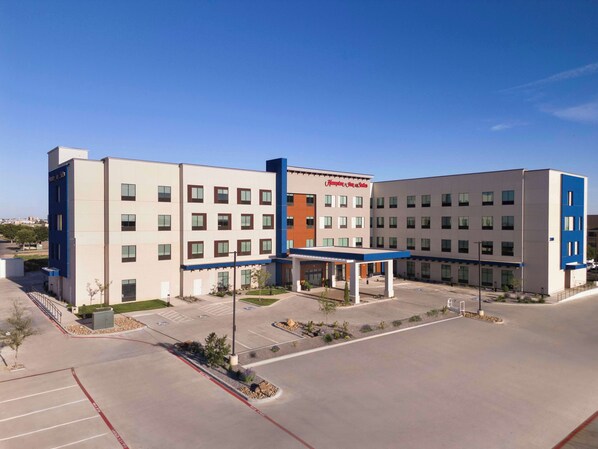 A modern hotel with a central courtyard, multiple parking spaces, and a clear sky. - Hampton Inn & Suites Amarillo West (Amarillo)