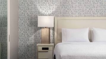 A hotel room with a patterned wallpaper, a bedside table with a lamp, and a neatly made bed.