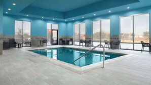 Une piscine intérieure aux murs d’un bleu éclatant et aux grandes fenêtres, entourée d’espaces de détente et offrant une vue sur l’extérieur.