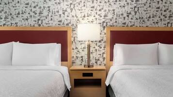 A hotel room with two beds, a nightstand with a lamp, and a patterned wallpaper.