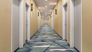 Un couloir d’hôtel avec un tapis à motifs, des portes blanches et un éclairage encastré.