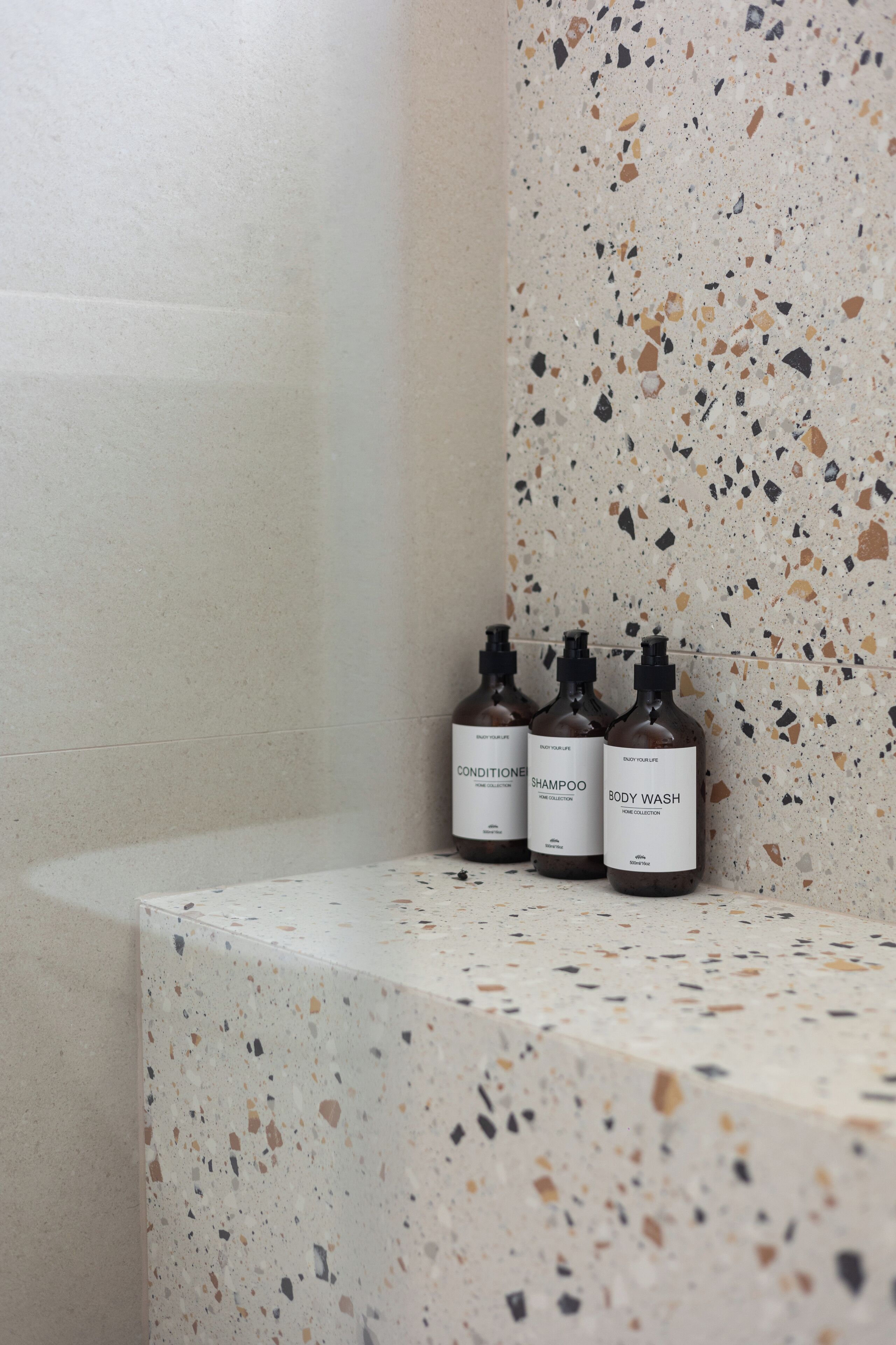 Three bottles of body wash on a speckled countertop in a bathroom.