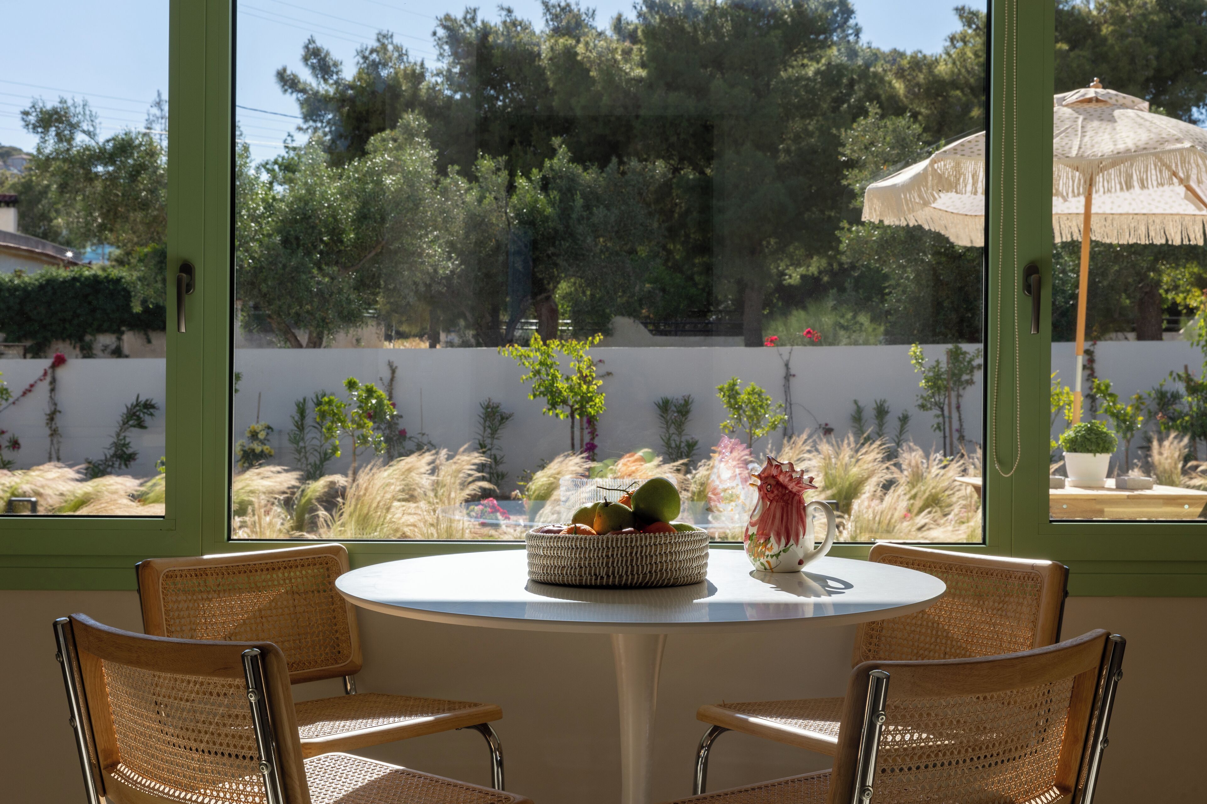 A round table with wicker chairs, a fruit bowl, and a decorative vase.