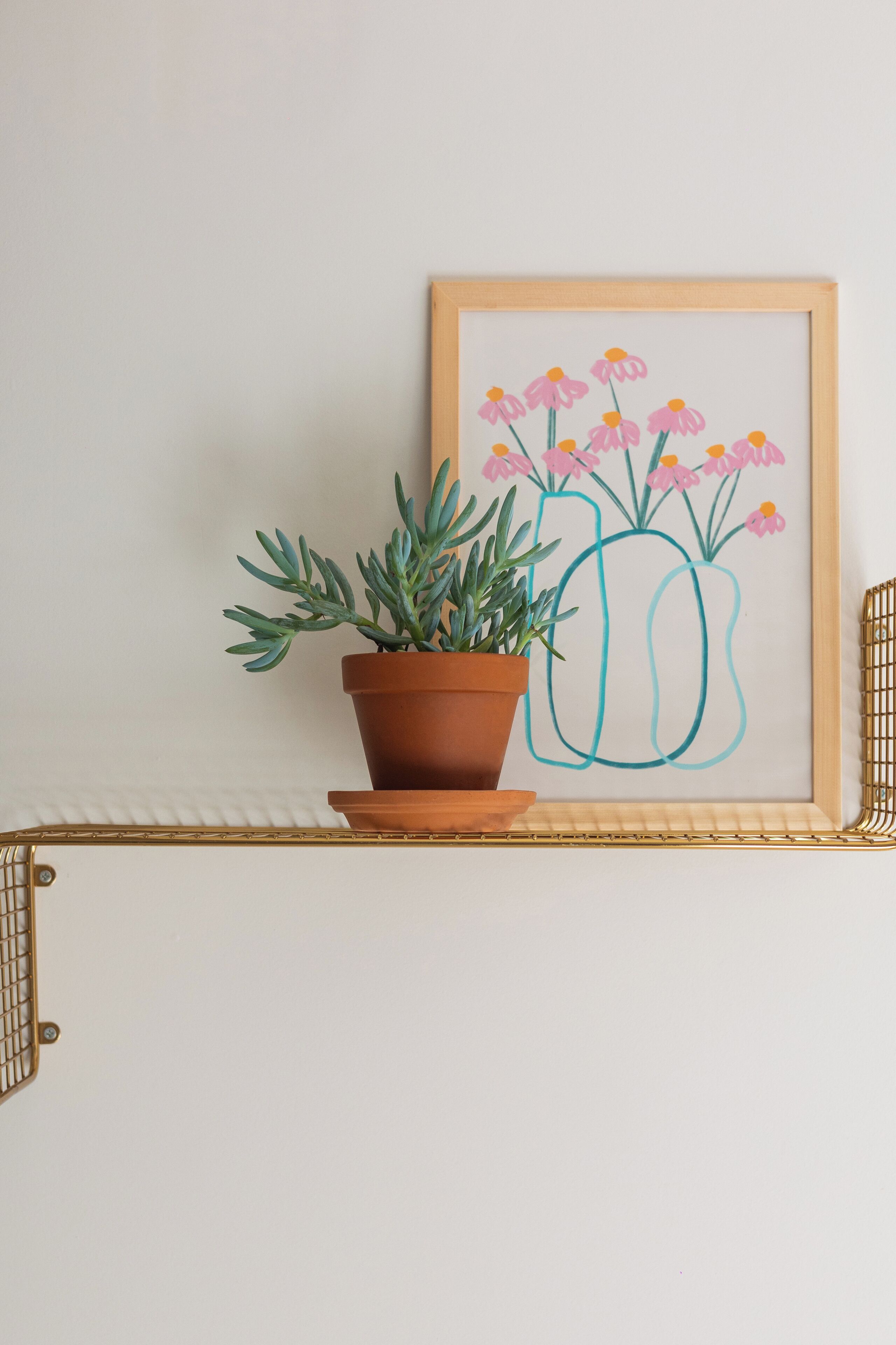 A potted plant on a shelf with a framed artwork of flowers.