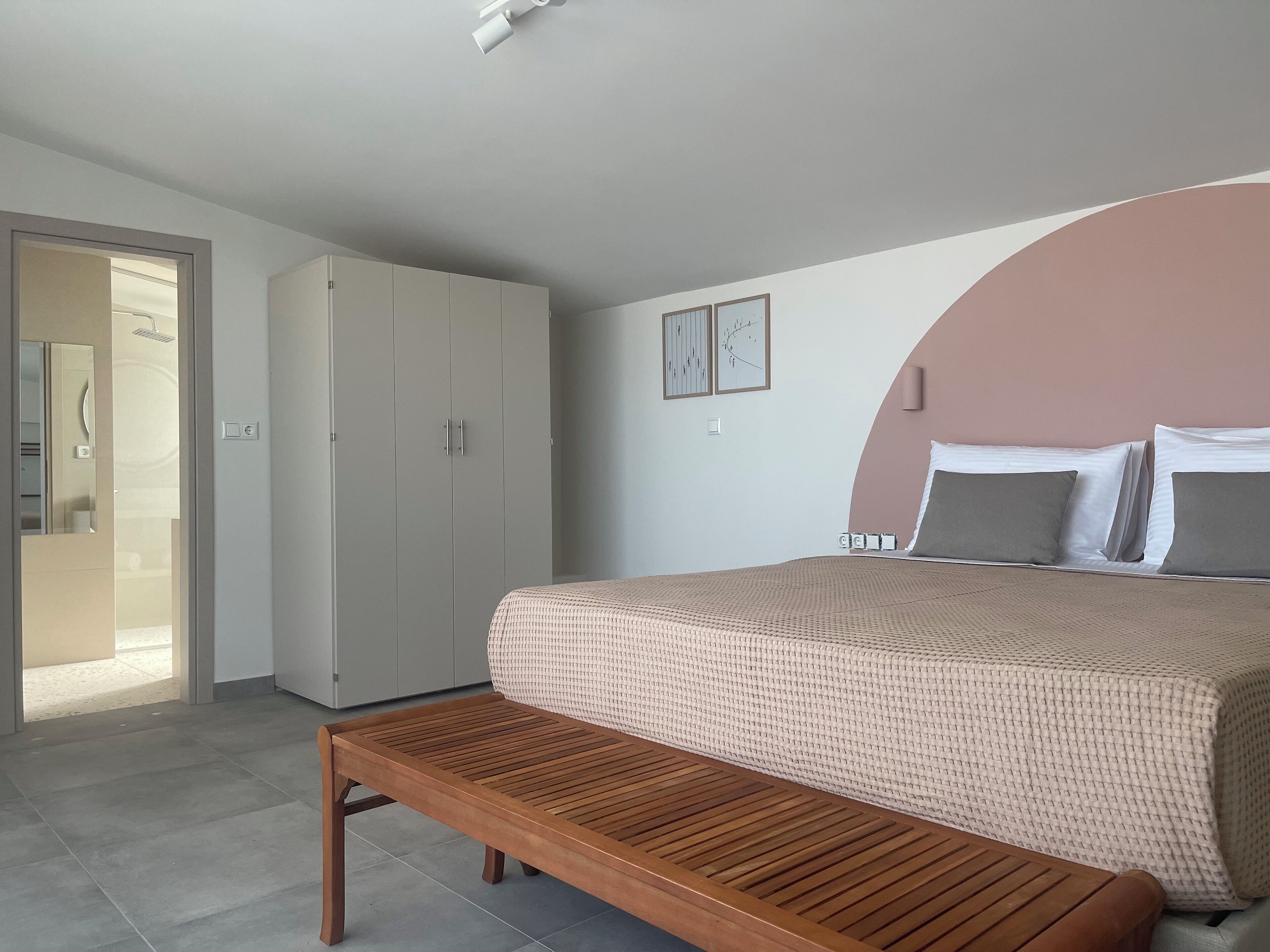 Un dormitorio con cama, un banco de madera, un armario y un baño visible a través de una puerta abierta.