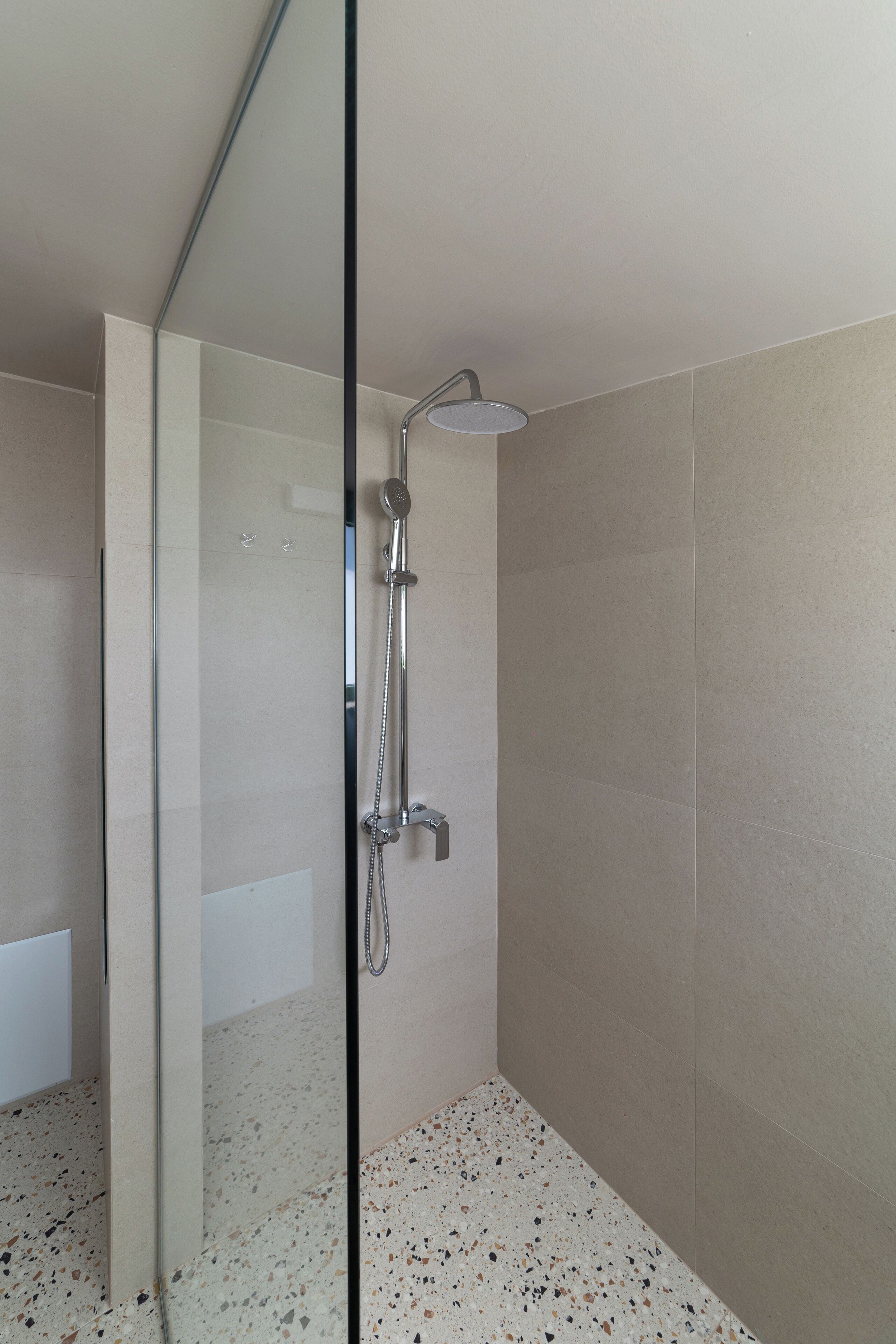 A modern shower with a glass door, a handheld showerhead, and a wall-mounted control.
