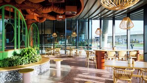 Ein modernes Restaurant-Interieur mit großen Fenstern, Holzmöbeln und außergewöhnlichen Pendelleuchten.