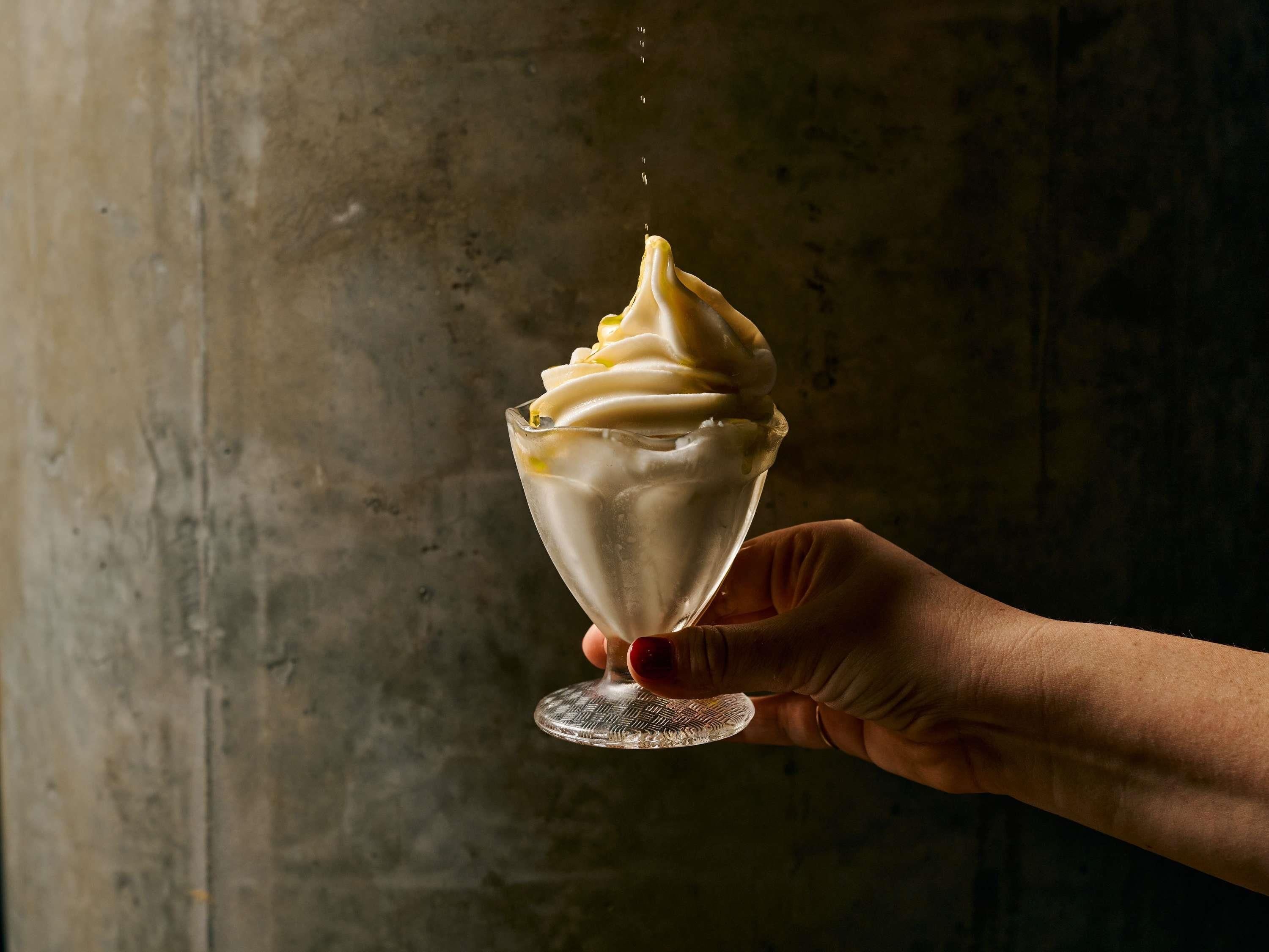 Una mano sosteniendo un vaso de helado con una voluta cremosa.