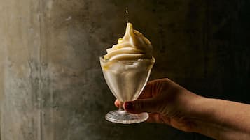 Une main tenant un verre de crème glacée surmontée d'une spirale crémeuse.