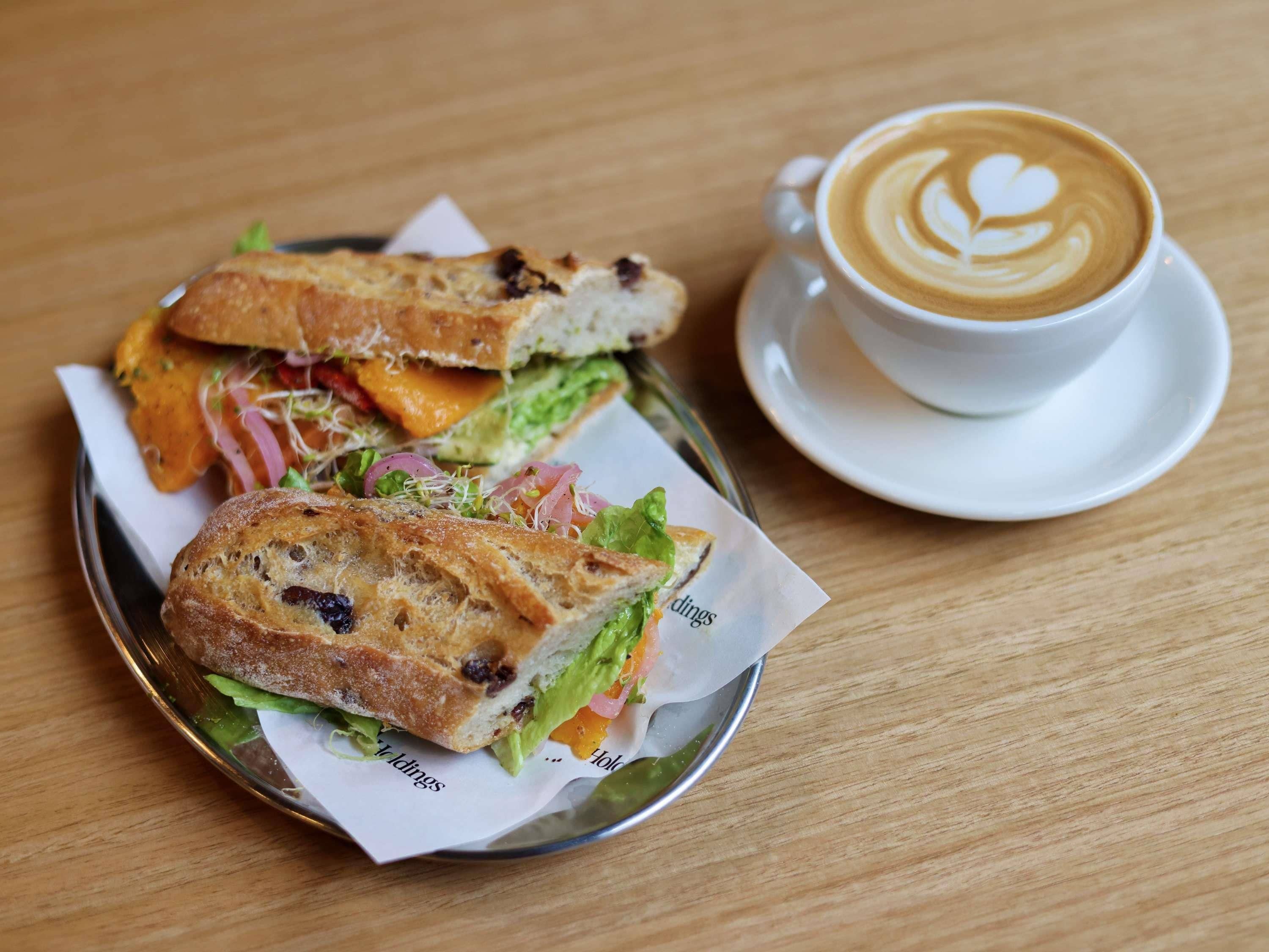 A sandwich on a plate with a cup of coffee on a saucer.